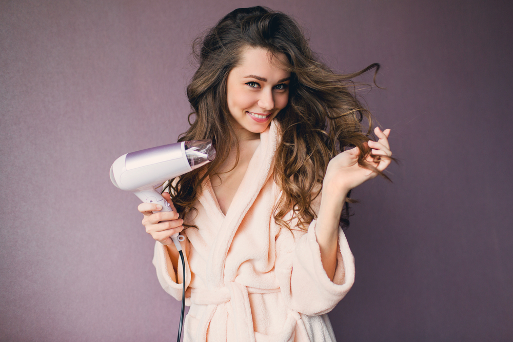 Beautiful young woman holding hair blow dry